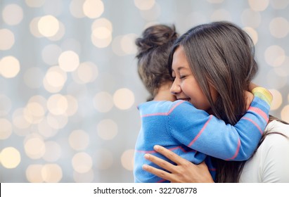family, children, love and happy people concept - happy mother and daughter hugging over lights background