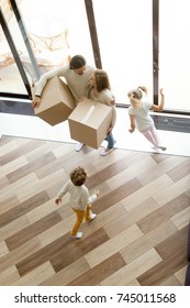 Family And Children Moving Into New Home, Kids Playing Running Around Parents Holding Boxes Standing In House Hall Together, Happy Couple With Two Children Having Fun Move In, Vertical Top View