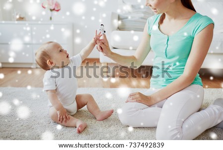 family, children and parenthood concept - happy smiling young mother and baby playing with finger puppet at home over snow