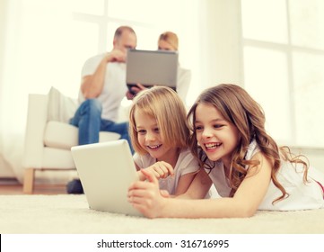 family, children, technology and home concept - smiling sister with tablet pc computer and parents on the back with laptop - Powered by Shutterstock