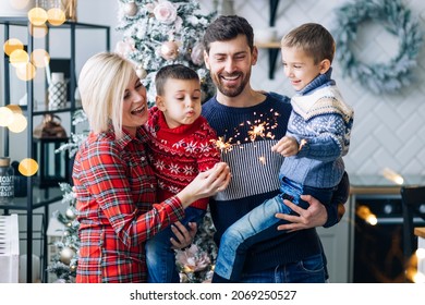family, christmas, holidays and people concept - happy mother, father and children with sparklers hugging celebrating new year.