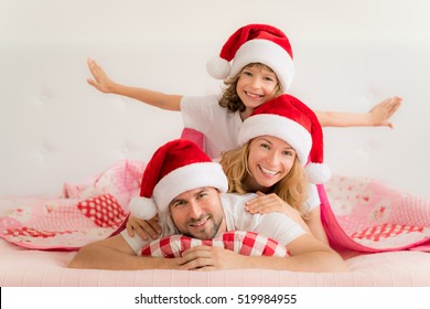 Family In Christmas Santa Hats Lying On Bed. Mother; Father And Baby Having Fun In Bedroom. People Relaxing At Home. Winter Holiday Xmas And New Year Concept