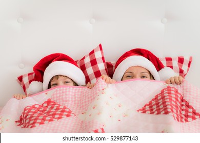 Family In Christmas Santa Hats Lying On Bed. Mother And Daughter Having Fun In Bedroom. People Relaxing At Home. Winter Holiday Xmas And New Year Concept