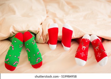 Family In Christmas Socks Lying On Bed. Mother, Father And Baby Having Fun Together. People Relaxing At Home. Winter Holiday Xmas And New Year Concept