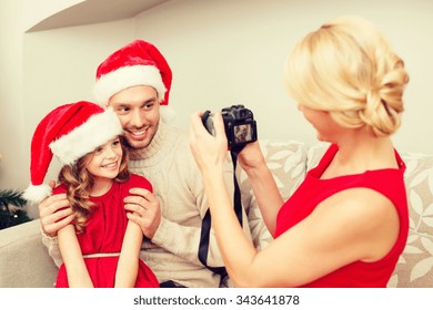 Family, Christmas, X-mas, Happiness And People Concept - Mother Taking Picture Of Smiling Father And Daughter In Santa Helper Hats