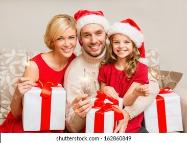 Family, Christmas, X-mas, Winter, Happiness And People Concept - Smiling Family In Santa Helper Hats With Many Gift Boxes And Bengal Lights