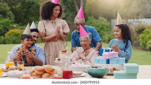 Family, clapping hands and happy with hat at birthday party for celebration, surprise or sparkler in garden of home. Grandparents, parents and kids with applause for gathering and event in backyard - Powered by Shutterstock