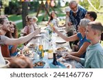 Family clinking glasses at summer garden party. Celebratory toast at the table.