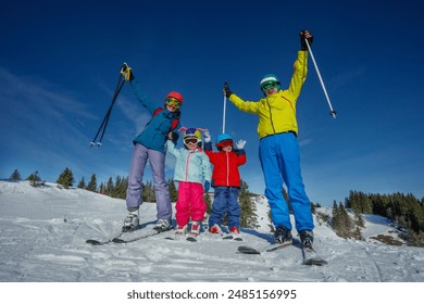 A family in colorful ski outfits stands on a sunlit, snowy hill, ready for skiing lifting hands - Powered by Shutterstock