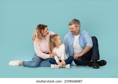 Family Communication. Happy Middle Aged Parents Talking To Little Daughter Laughing Together Sitting Over Blue Background. Joy Of Parenthood. Studio Shot, Full Length