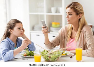 Family, Communication And People Concept - Sad Girl Looking At Her Mother With Smartphone Having Dinner At Home
