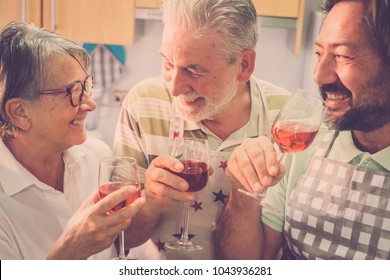 Family Composed By Father And Mother Senior Adult Aged And Son Middle Age 45 Years Old. Together Having Fun At Home In The Kitchen Drinking Some Red Wine For Cocktail Time. Everybody Smiling And Fun.