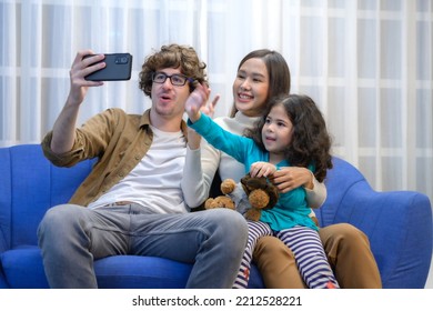 Family Concept : Father And Mother And  Daughters Were Laughing Happily And Wave To Say Hello To His Friends Or Relatives By Making A Video Call Via The Mobile Phone In The Living Room.