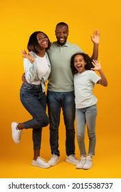 Family Concept. Happy African American Man, Woman And Girl Waving Hands To Camera And Smiling, Posing For Photo Over Yellow Background, Studio Shot, Crop. Full Length