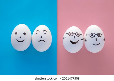 Family Concept No People. Two Couples With Different Emotions. One Pair Of Eggs In Glasses On A Pink Background, Holding Hands And Smiling. The Second Couple Is On A Blue Background, Separated And Sad