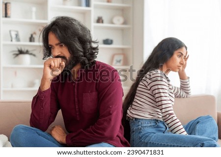 Family Conflict Concept. Stubborn couple sit on couch back to back avoid talking after fight, offended indian man and woman separated on sofa ignoring one another, husband and wife not looking in eyes