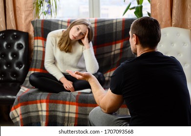 Family conflict of man and young woman at home. They are sitting in the room and talking displeased. Focus on the man who sits with his back to the camera.