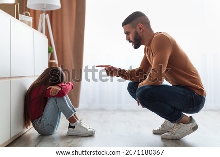 Family Conflicts And Punishment Concept. Profile Of Angry Annoyed Father Scolding His Upset Crying Little Daughter For Her Behaviour While She Sitting On The Floor At Home. Naughty Kid, Children Abuse