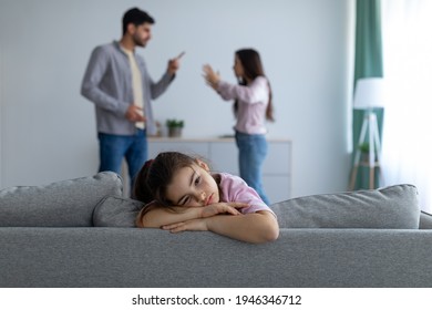 Family conflicts. Sad arab girl sitting alone, feeling lonely and depressed while her parents arguing on the background, selective focus. Family crisis and relationship problems