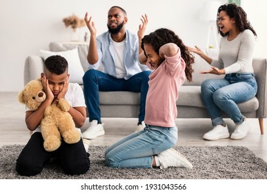 Family Conflicts. Sad little black children covering ears with hands while their parents arguing in the background, upset boy and girl don't want to hear quarrel, stressed kid sitting on the floor - Powered by Shutterstock