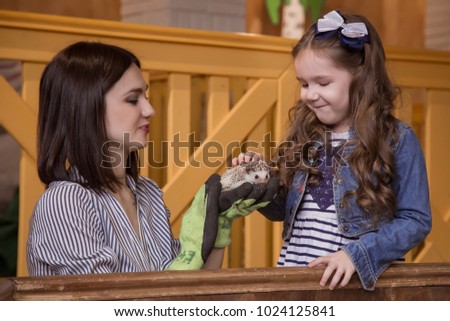 Family in the contact zoo, mother and daughter holding an African hedgehog. Hands in protective gloves.