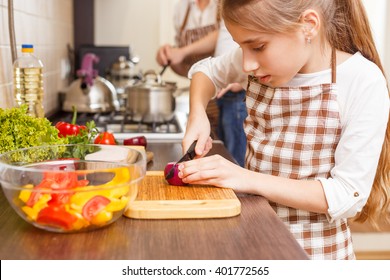 Family cooking background. Small girl cutting onion preparing salad at the kitchen counter