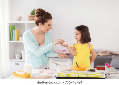 Family, Cooking, Baking And People Concept - Happy Mother And Little Daughter Holding Egg And Making Cupcakes At Home Kitchen