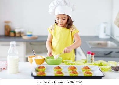 Family, Cooking, Baking And People Concept - Little Girl In Chefs Toque Making Batter For Muffins Or Cupcakes At Home Kitchen