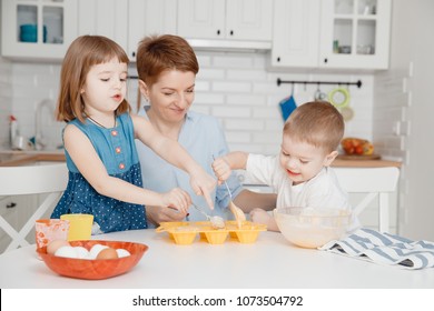 Family cooking. Children and mom prepare cupcakes. They laugh and smile, homemade cakes. White kitchen.