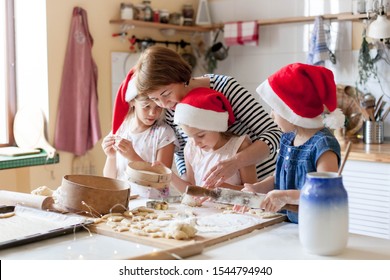 Family Is Cooking Christmas Gingerbread Cookies In Cozy Home Kitchen For Holiday Dinner. Funny Kids And Woman Bake Xmas Biscuits. Mother Is Teaching Daughters. Lifestyle Moment. Children Chef Concept.