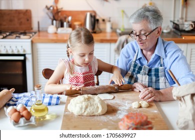 Family Cooking At Home. Grandmother And Child Making Italian Food And Meal In Cozy Kitchen. Senior Woman And Little Girl Baking, Using Rolling Pin. Cute Kid Helping To Prepare Dinner. Children Chef.