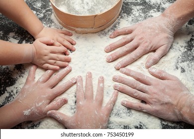 Family Cooking Homemade Cakes, Mom's Hands And Two Daughters In Flour On A Black Table Background.