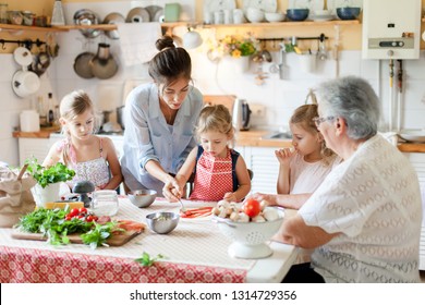 Family Are Cooking Italian Pizza Together In Cozy Home Kitchen. Cute Kids, Mother And Grandmother Are Preparing Food For Dinner. Women Are Teaching Three Girls. Cooking Class, Children Chef Concept.