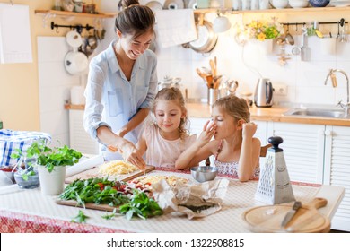 Family are cooking italian pizza together in cozy home kitchen. Cute kids with happy mother are preparing food for dinner and eating cheese. Two girls are helping woman. Lifestyle moment. - Powered by Shutterstock