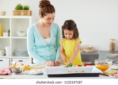 family, cooking and people concept - happy mother and little daughter with molds making cookies from dough at home kitchen