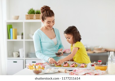 Family, Cooking And People Concept - Happy Mother And Little Daughter Making And Decorating Cupcakes With Chocolate Sprinkles At Home Kitchen