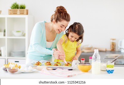 Family, Cooking And People Concept - Mother And Little Daughter Making And Decorating Cupcakes With Cream Frosting At Home Kitchen