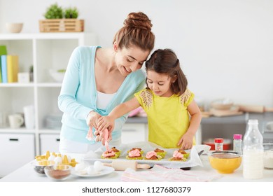 Family, Cooking And People Concept - Mother And Little Daughter Making And Decorating Cupcakes With Cream Frosting At Home Kitchen