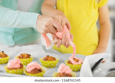 Family, Cooking And People Concept - Mother And Little Daughter Making And Decorating Cupcakes With Cream Frosting At Home Kitchen