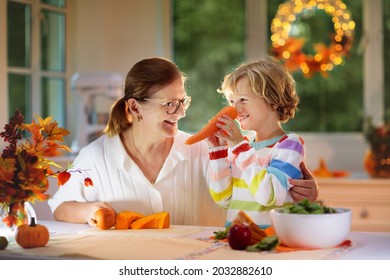 Family Cooking Thanksgiving Dinner. Mother And Child Cut Pumpkin In Decorated Kitchen. Mom And Kid Cook Vegetable Meal In Autumn. Cozy Indoor Evening In Dining Room. Fall Season Food.