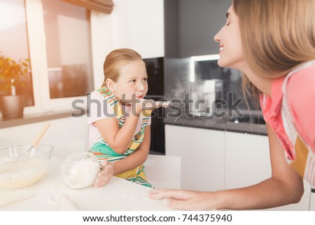 The family cooks dough for baking. Mom and daughter are preparing dough and fooling around. The dough is in a bowl next to them. A woman and a girl are in the modern kitchen.
