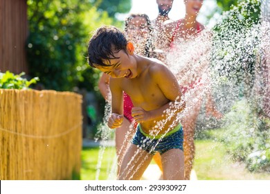 Family Cooling Down With Sprinkler In Garden, Lots Of Water Splashing Around