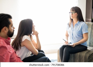 Family Counselor Talking With Couple In Her Office. Female Psychologist Helping Hispanic Couple With Problem.