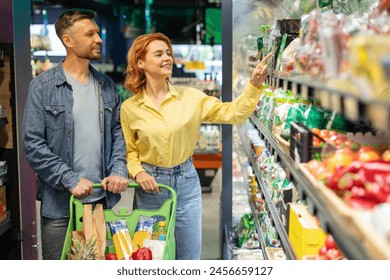 Family couple choosing food in supermarket, shopping groceries, woman pointing fingers at fresh vegetables. Consumers buying products in grocery store - Powered by Shutterstock