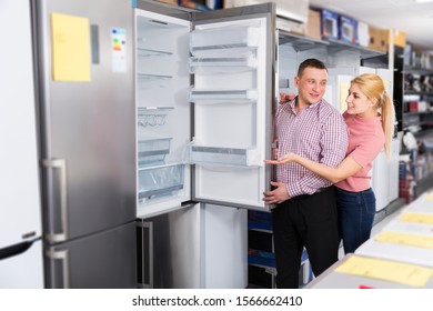Family couple choosing fridge in store of household appliances