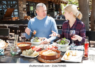 Family Couple Enjoying Warm Spring Day And Delicious Dinner With Wine In Cosy Country Restaurant In Open Air