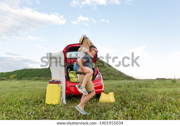 Family couple having fun at the\
campsite rolling each other on their hands running on the green\
grass on a summer day in the background of a car with Luggage\
things