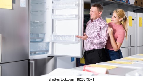 Family Couple Looking New Refrigerator In Household Appliances Store..