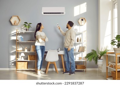La pareja familiar utiliza un práctico sistema de aire acondicionado en casa. Joven marido y mujer instalando una temperatura cómoda en su moderno aire acondicionado de CA en la pared del salón