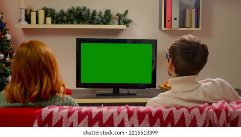 Family Couple Watching Green Screen TV Mockup Sitting On Couch In Living Room Together. Rear View On Casual People Who Watching TV Green Screen. TV Show Or News In Home Rest